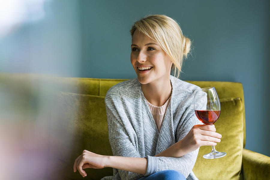 Happy woman holding glass of red wine on sofa Photograph by Portra