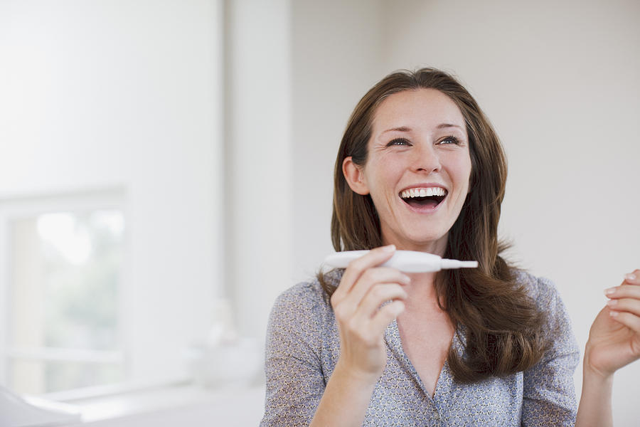 Happy woman holding pregnancy test Photograph by Tom Merton