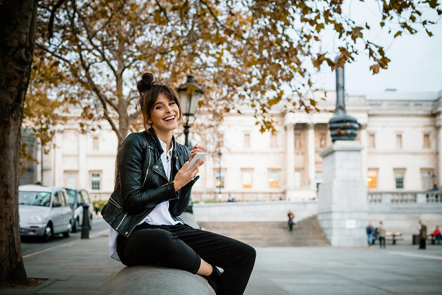 Happy woman using smart phone at Trafalgar Square in London, autumn season Photograph by Izusek
