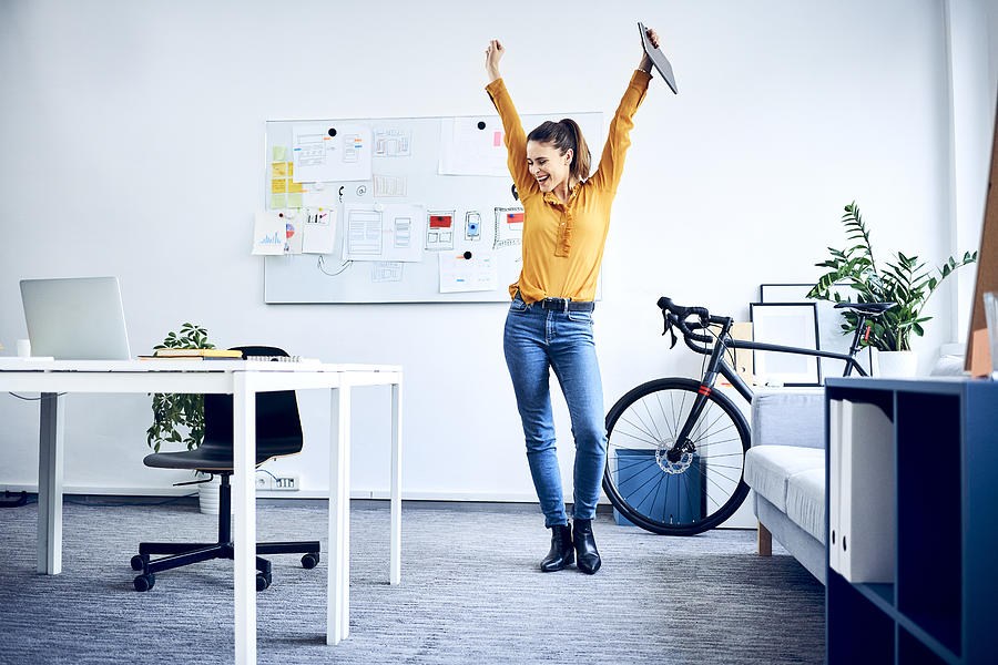 Happy young businesswoman cheering in office Photograph by Westend61