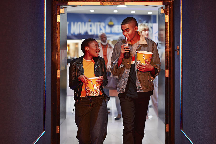 Happy young friends talking while walking in corridor at movie theater Photograph by Klaus Vedfelt