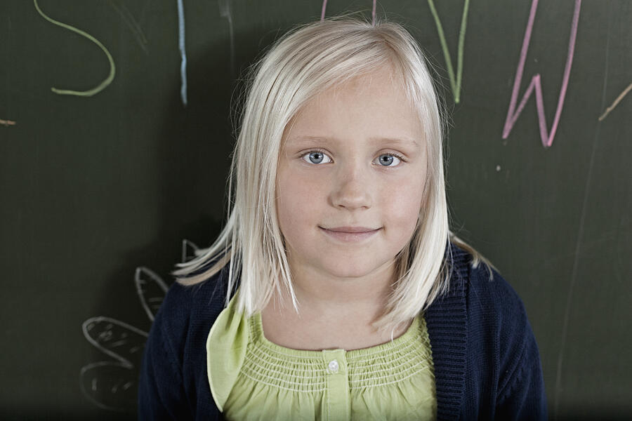 Happy young schoolgirl (8-9) posing against blackboard Photograph by Oliver Rossi