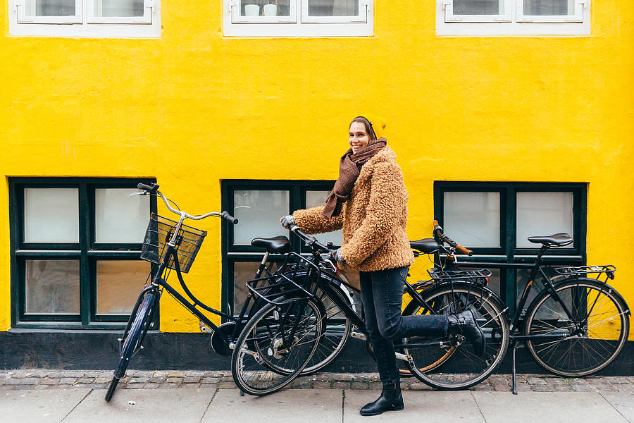 Happy young smiling woman with bicycle against yellow wall in Copenhagen Photograph by Alexander Spatari