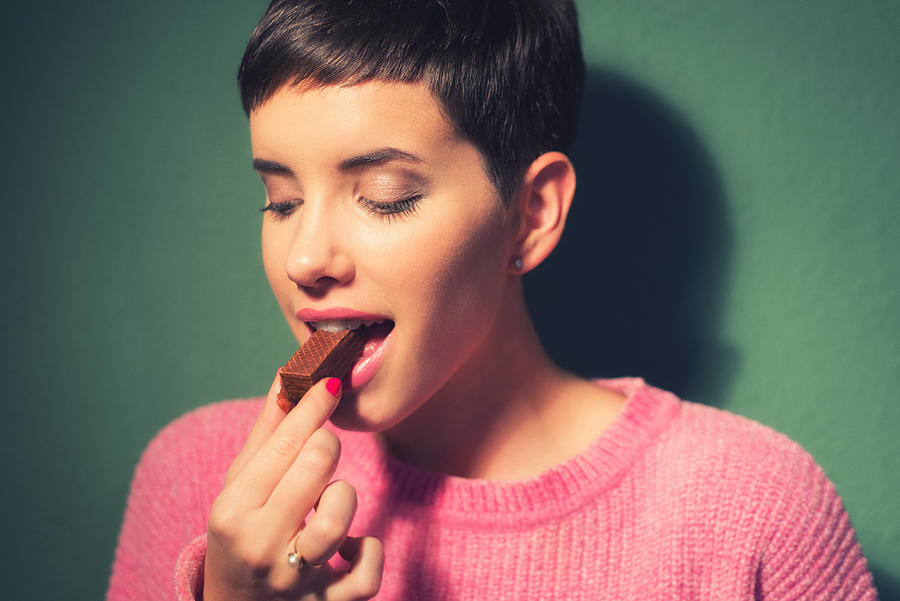 Happy young woman eating chocolate cookie Photograph by Slavica
