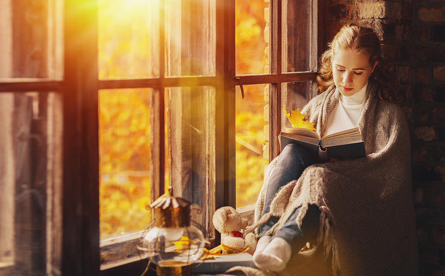 Happy young woman reading book by window in fall Photograph by Evgenyatamanenko