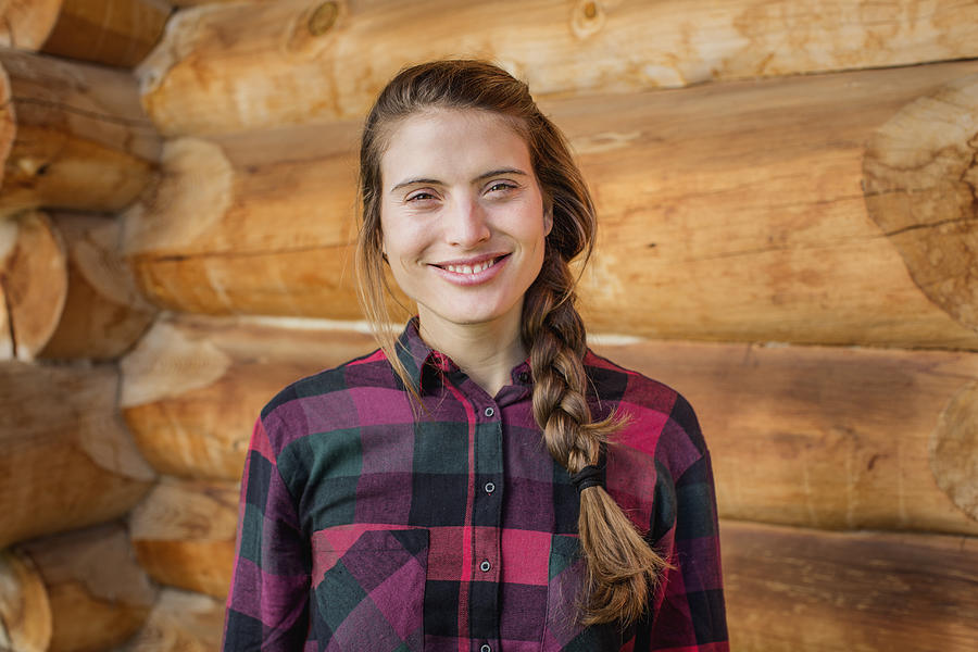 Happy young woman standing against log cabin Photograph by Morsa Images