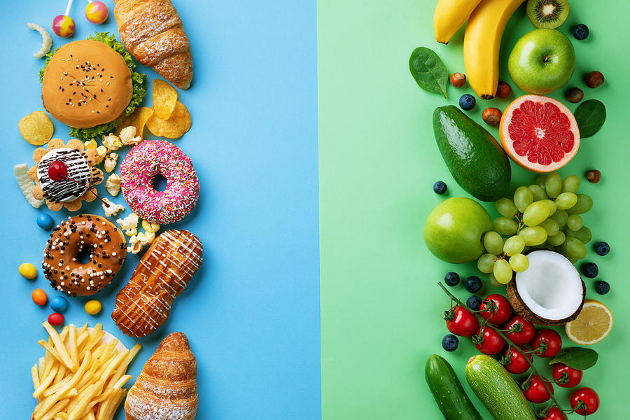 Healthy and unhealthy food background from fruits and vegetables vs fast food, sweets and pastry top view. Diet and detox against calorie and overweight lifestyle concept. Photograph by Julia_Sudnitskaya