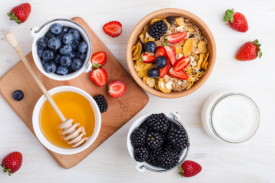 Healthy breakfast with cereal, fresh berries, yogurt and honey over white rustic wooden table viewed from above Photograph by Istetiana