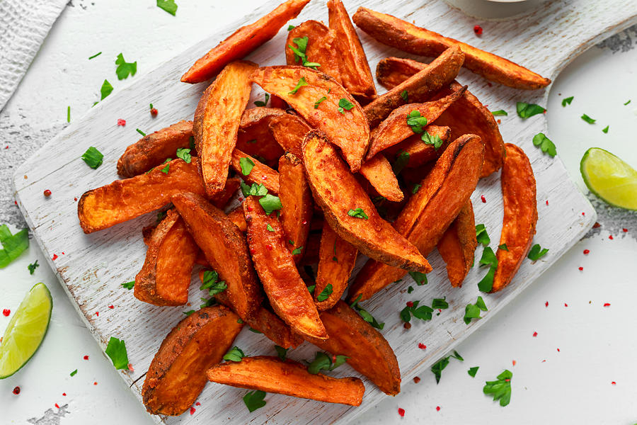 Healthy Homemade Baked Orange Sweet Potato wedges with fresh cream dip sauce, herbs, salt and pepper Photograph by DronG
