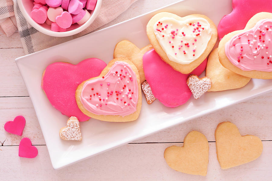 Heart shaped Valentines Day cookies with pink and white icing, overhead on a plate against white wood Photograph by Jenifoto