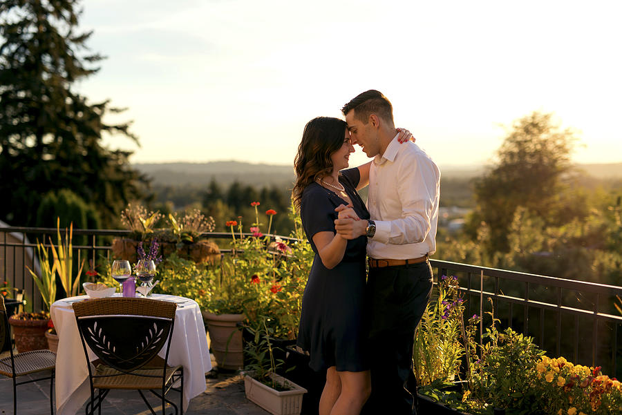 Heterosexual couple dancing after a romantic dinner on a veranda Photograph by FatCamera