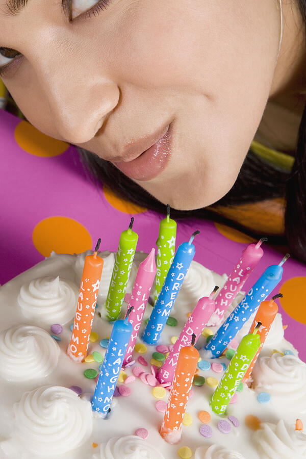 High angle view of a young woman blowing candles on a birthday cake Photograph by Glowimages