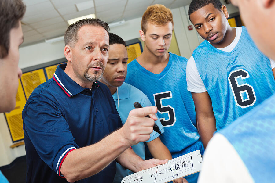 High school coach instructing basketball players in locker room Photograph by SDI Productions