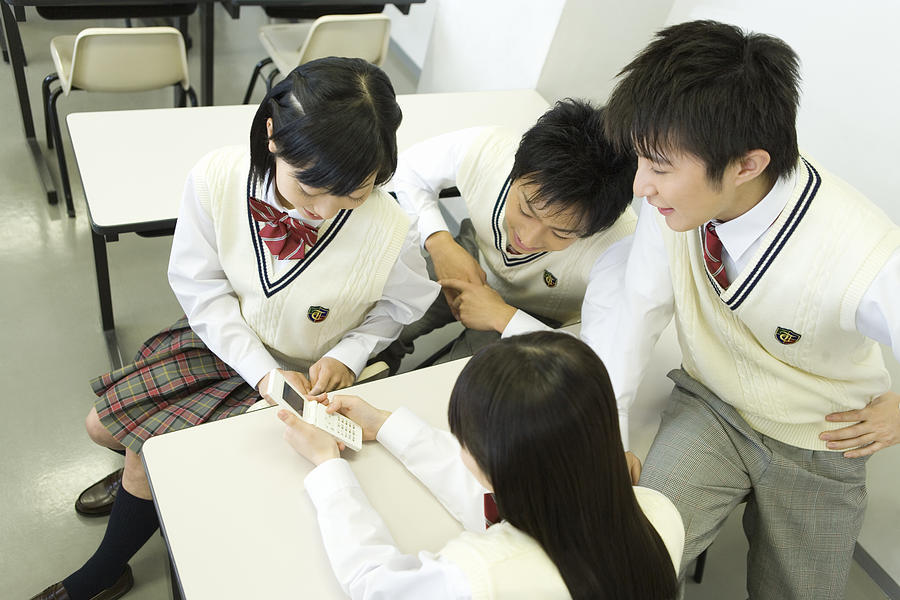High school students sitting at desk and looking at mobile phone in classroom Photograph by Daj