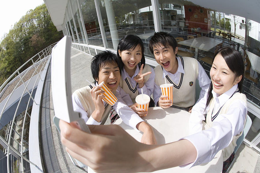 High school students smiling and photographing with mobile phone, fish-eye lens Photograph by Daj