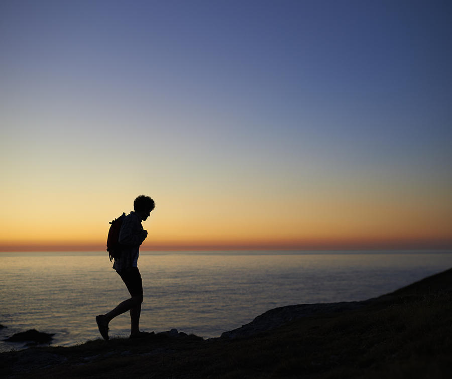 Hiker walking along coastline at sunset. Photograph by Dougal Waters