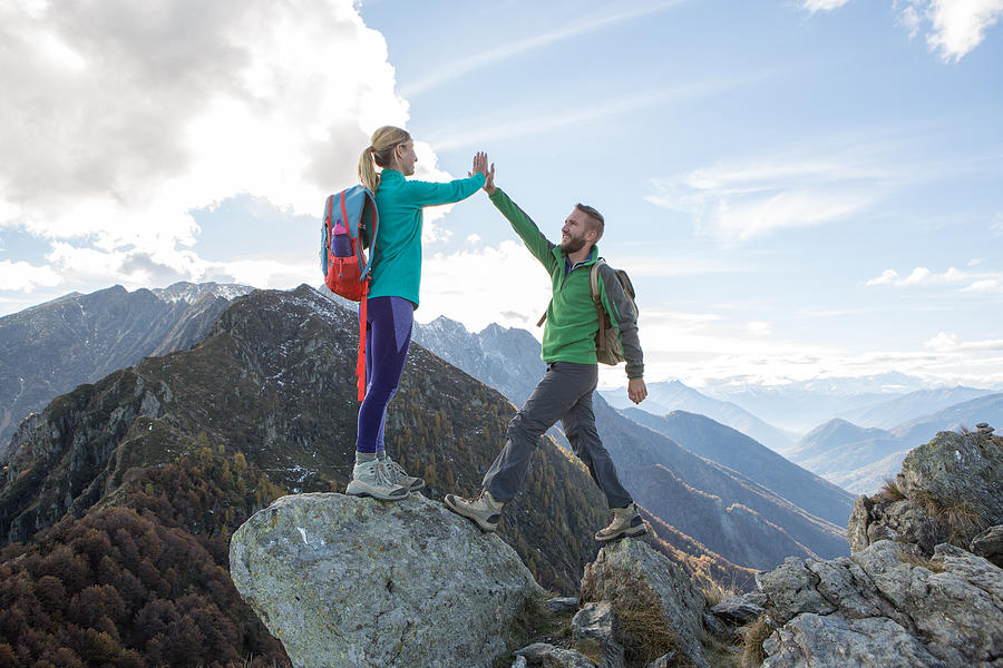 Hikers reaching mountain top celebrating with high five Photograph by Swissmediavision