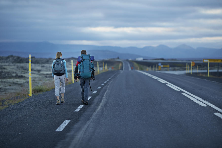 Hiking couple walking alonside long road Photograph by Klaus Vedfelt