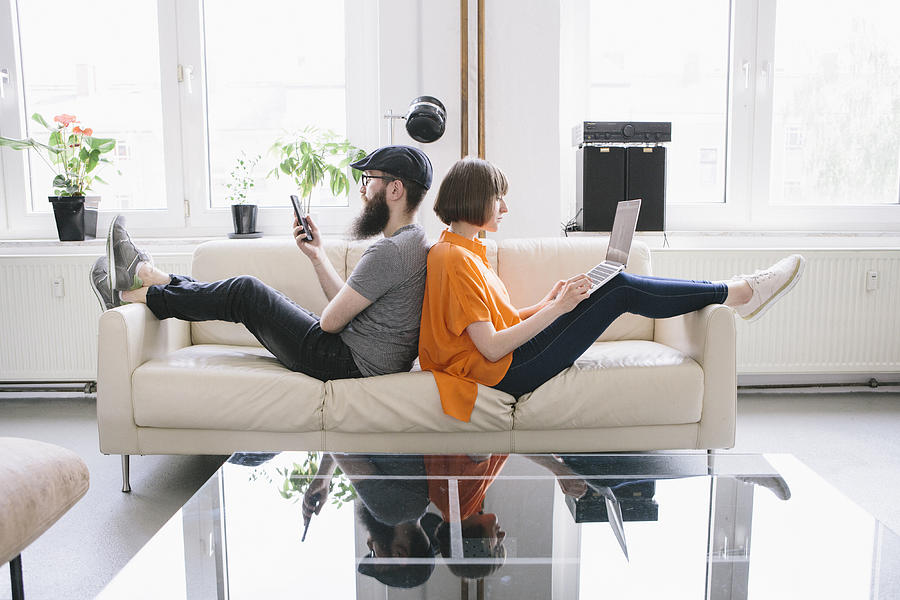 Hipster Couple Sit On Couch And Look Into Digital Devices Photograph by Fotografixx