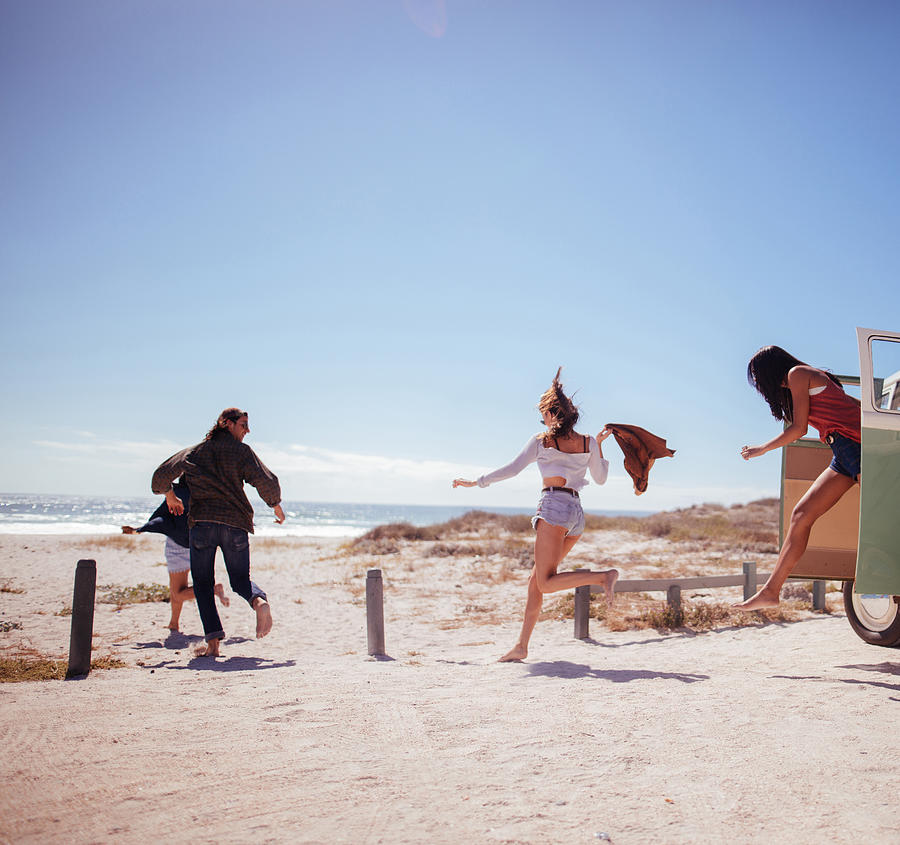 Hipster friends jumping out of Road Trip van at beach Photograph by Wundervisuals