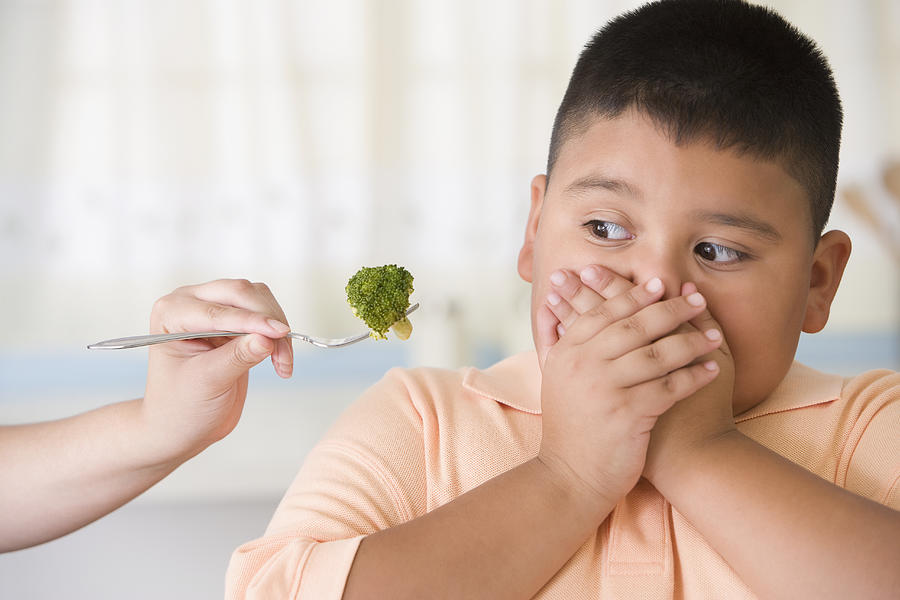 Hispanic boy covering mouth next to broccoli Photograph by Jose Luis Pelaez Inc