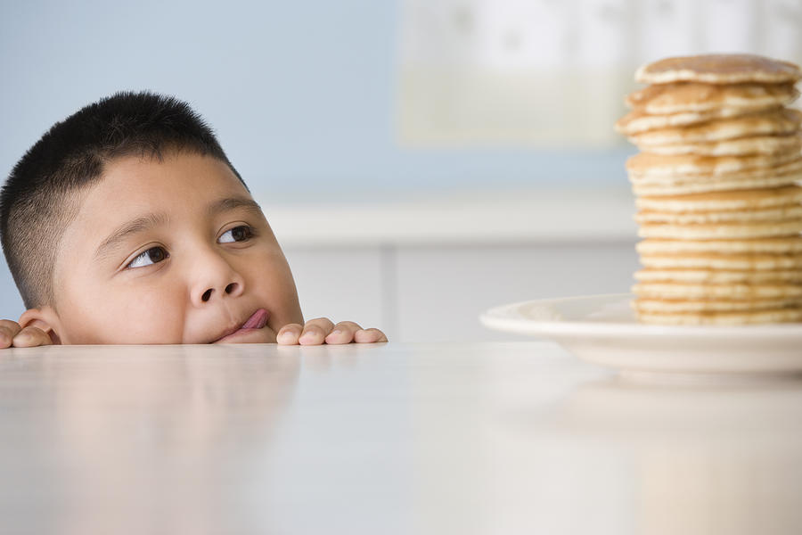 Hispanic boy licking lips at stack of pancakes Photograph by Jose Luis Pelaez Inc