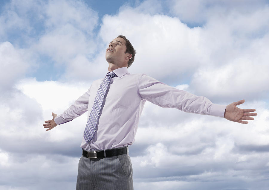 Hispanic businessman standing with arms outstretched under clouds Photograph by Jacobs Stock Photography Ltd