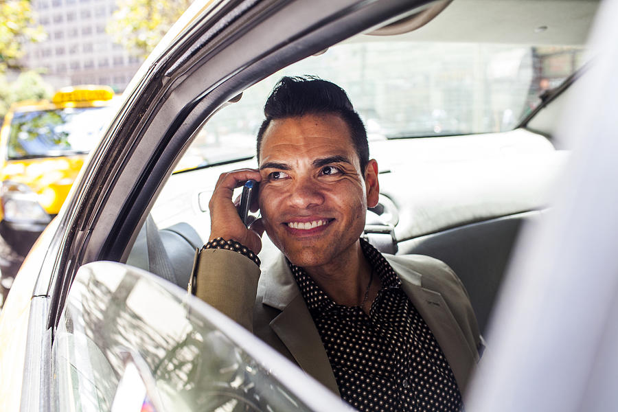 Hispanic businessman talking on cell phone in back seat of car Photograph by Adam Hester