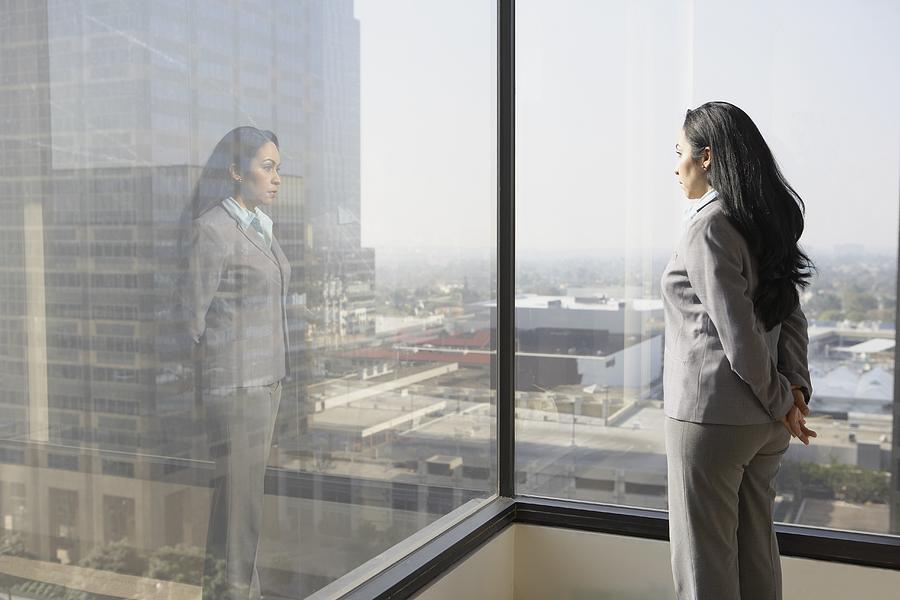 Hispanic businesswoman looking out a window Photograph by ER Productions Limited
