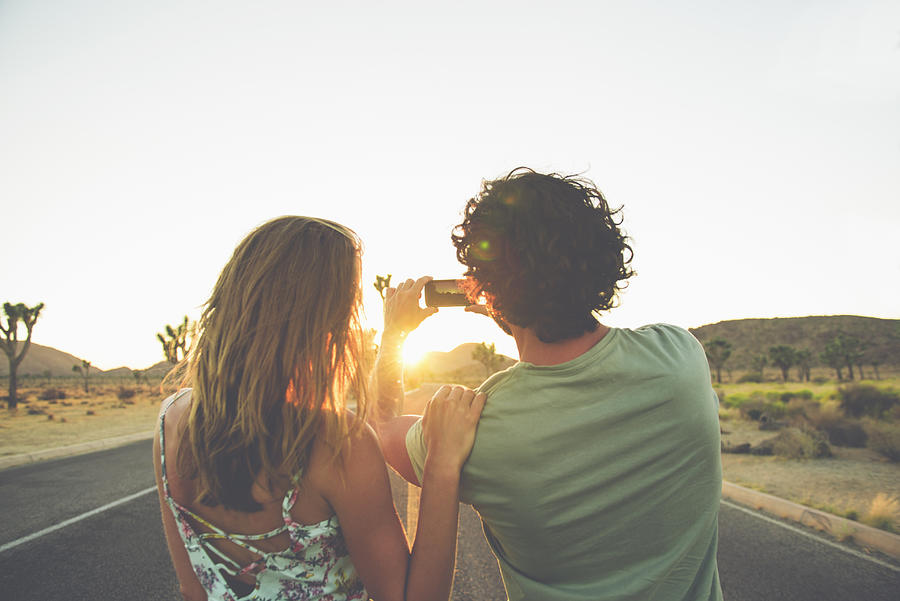 Hispanic couple photographing sunset in street Photograph by Jacobs Stock Photography Ltd