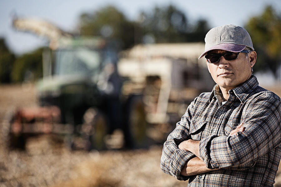 Hispanic farmer standing by harvester Photograph by Hill Street Studios