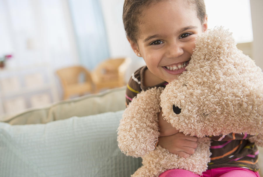 Hispanic girl hugging teddy bear on sofa Photograph by JGI/Jamie Grill