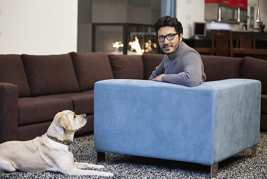 Hispanic man sitting in living room with dog Photograph by Hill Street Studios