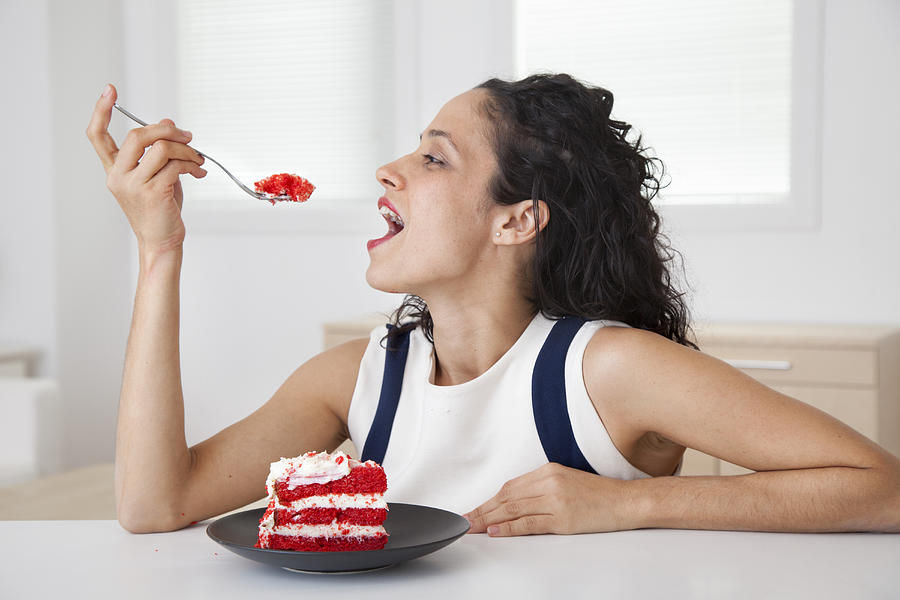 Hispanic woman eating cake in kitchen Photograph by Peter Dressel