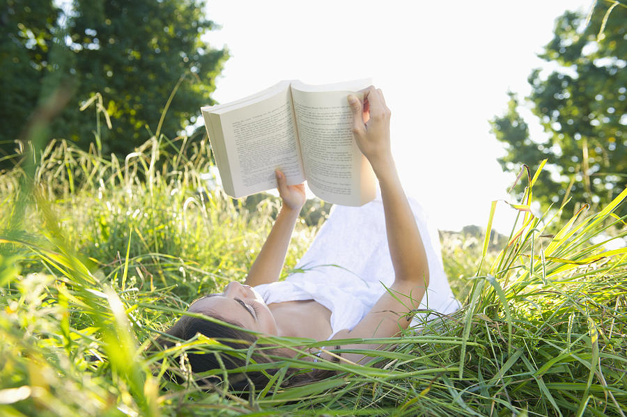 Hispanic woman laying in grass reading book Photograph by Jacobs Stock Photography Ltd
