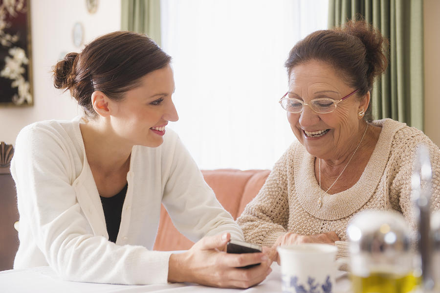Hispanic woman showing cell phone to grandmother Photograph by Jacobs Stock Photography Ltd