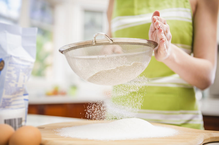 Hispanic woman sifting flour in domestic kitchen Photograph by Jacobs Stock Photography Ltd