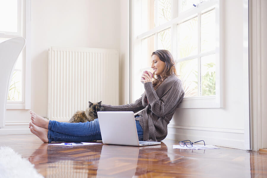 Hispanic woman sitting on floor with laptop and cat Photograph by Jacobs Stock Photography Ltd