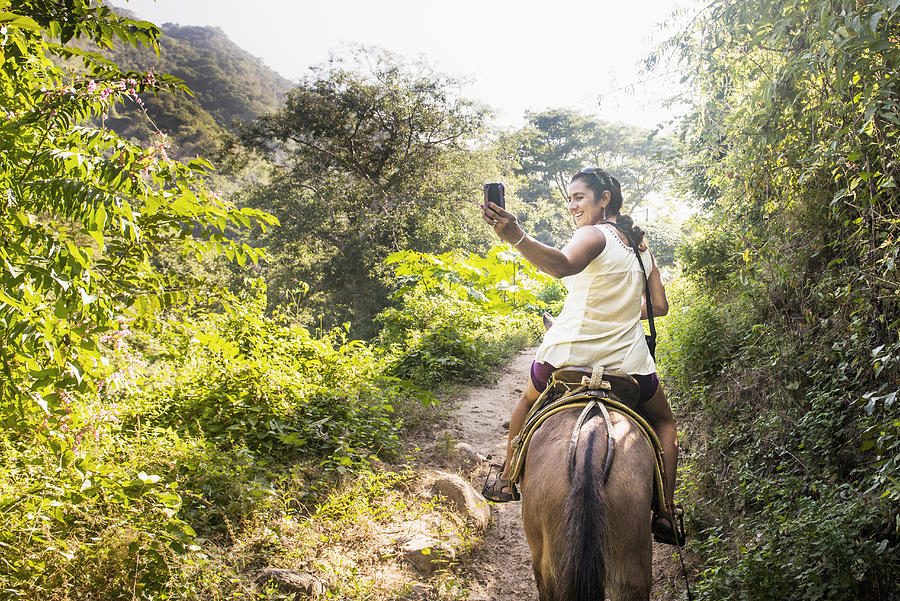 Hispanic woman taking pictures on horseback in jungle Photograph by Sollina Images