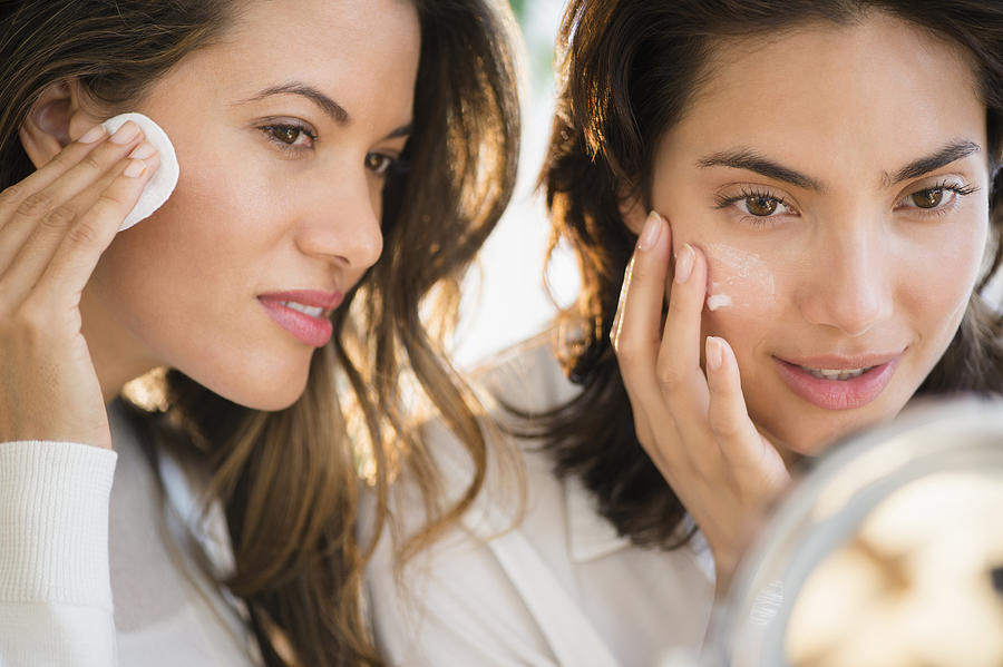Hispanic women applying makeup in mirror Photograph by JGI/Jamie Grill