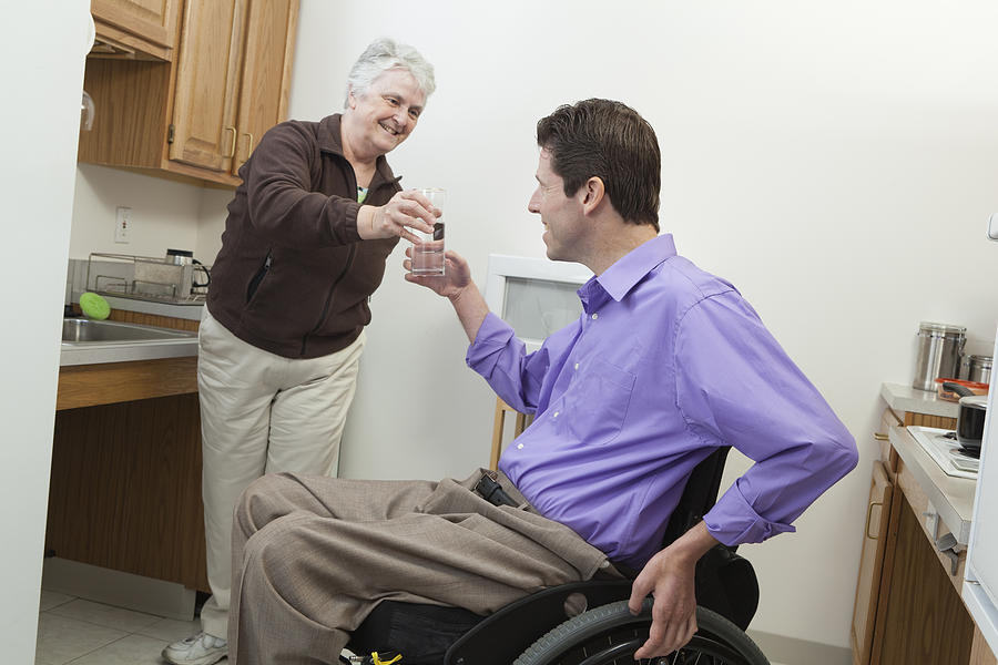 Home health aid offering a glass of water to a man in wheelchair with spinal cord injury Photograph by Huntstock