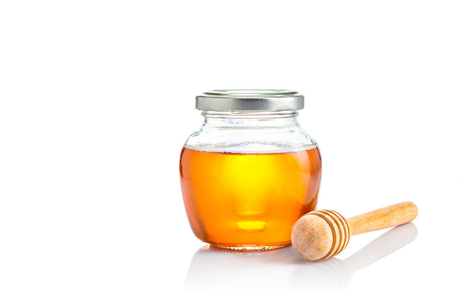 Honey in closed lid glass jar with wooden honey dipper at its side, all on white background with copy space Photograph by Yokaew