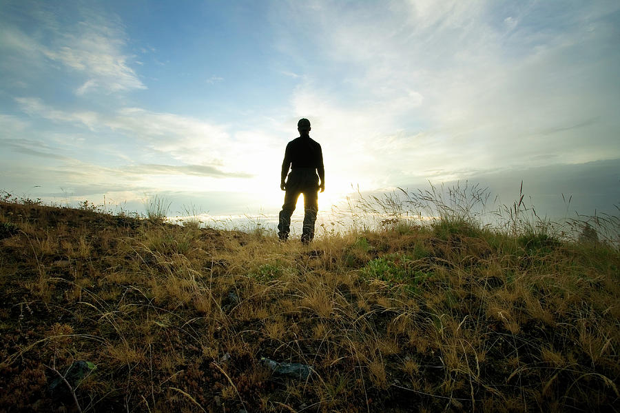 Human silhouette on a mountain ridge looking into the setting sun ...