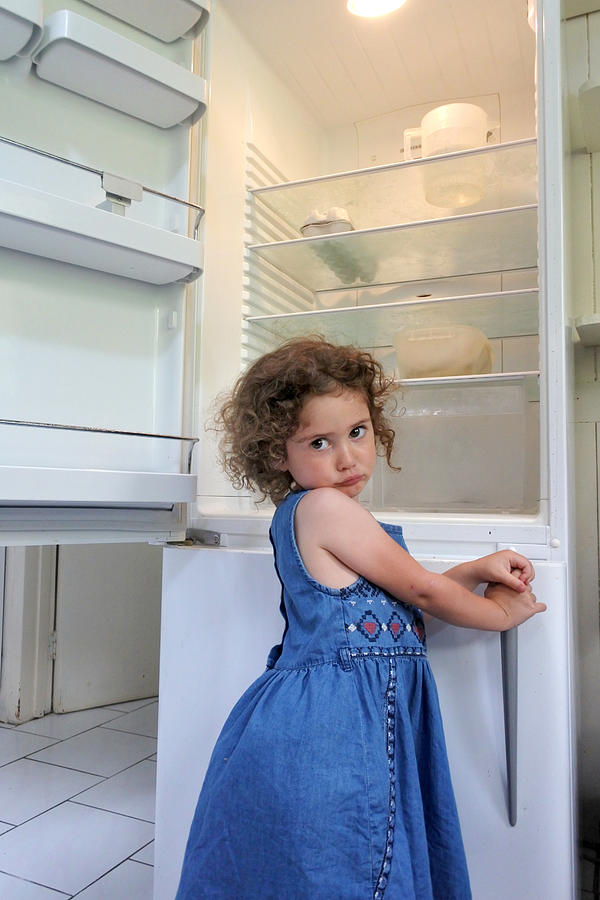 Hungry poor little girl looks for food in empty fridge at home Photograph by Rafael Ben-Ari