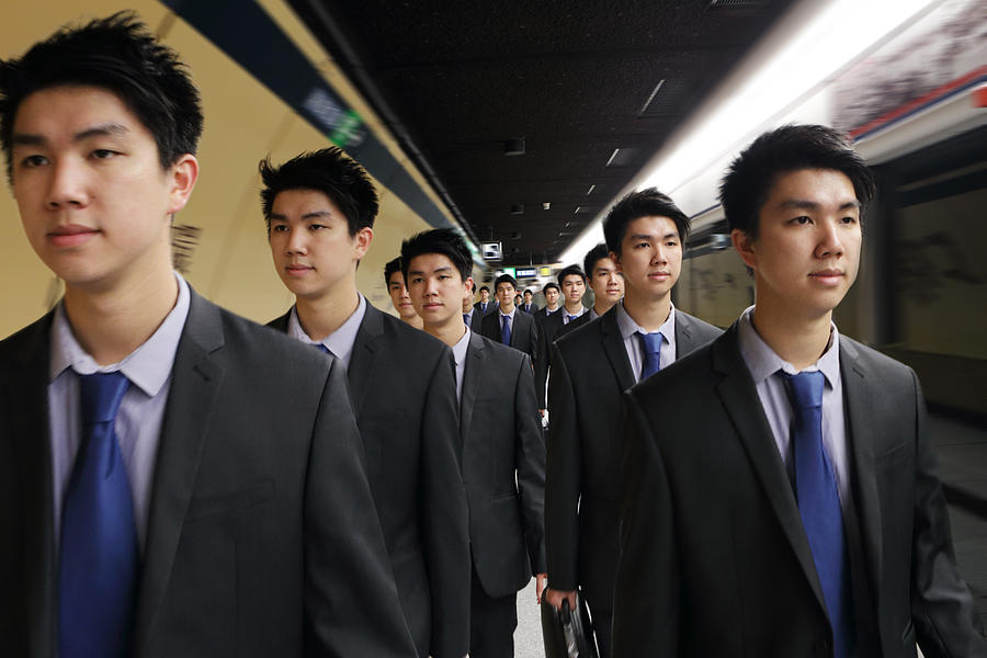 Identical men in suits walking along platform Photograph by Peter Cade