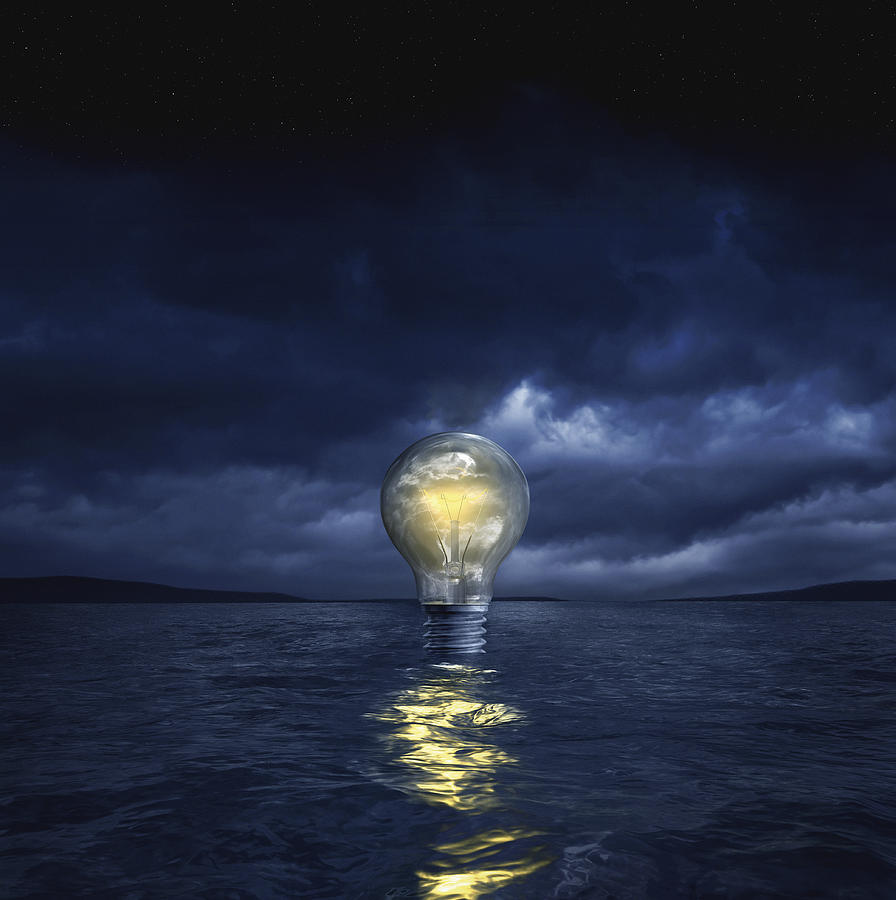 Illuminated light bulb floating in sea Photograph by Chris Clor