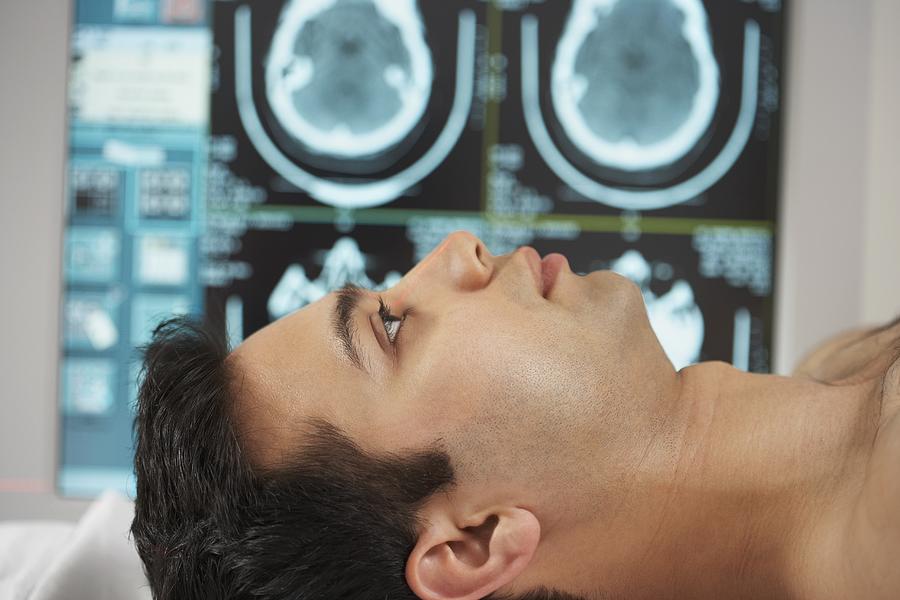 Indian male patient laying down with brain scans in background Photograph by ER Productions Limited