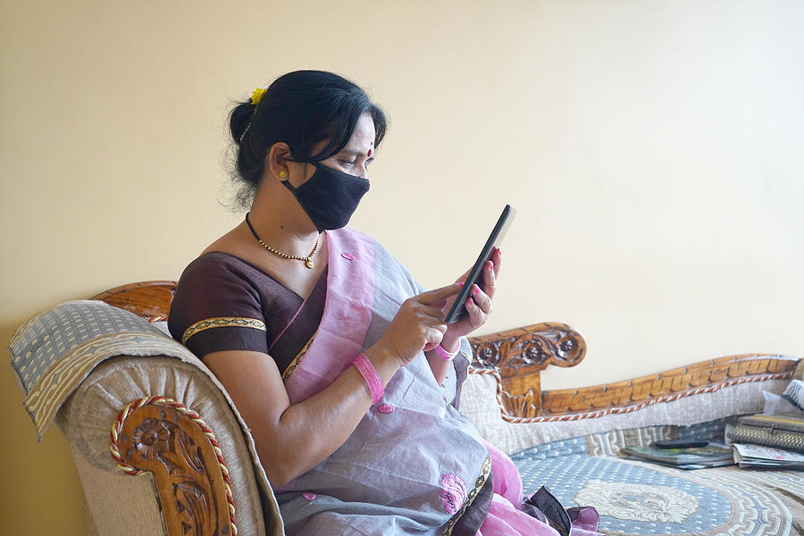 Indian woman with face protective mask reading news on tablet. Photograph by CR Shelare