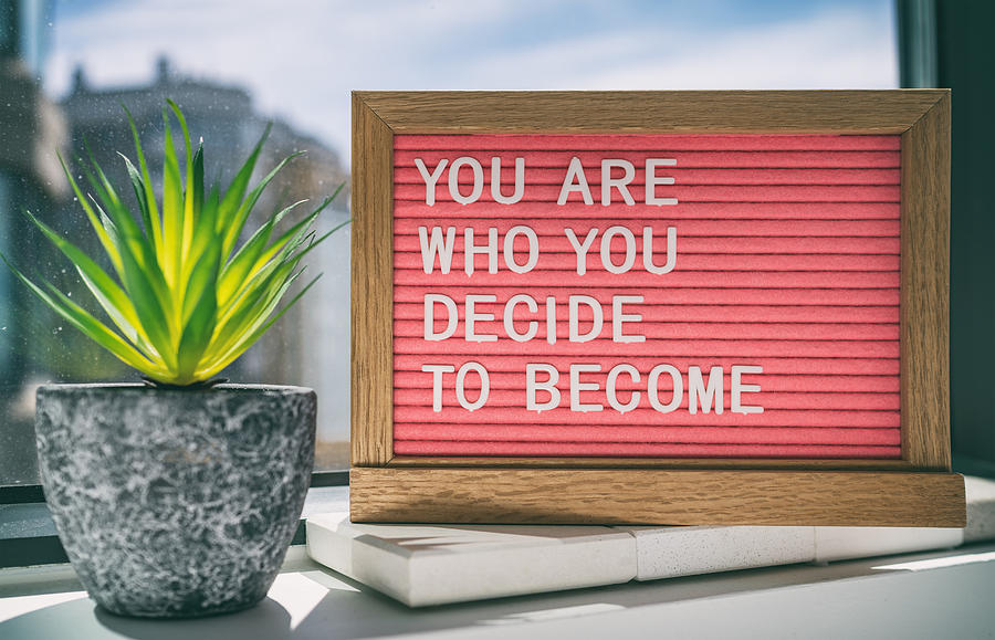 Inspiration quote message sign saying You are who you decide to become - life advice for self esteem, confidence. Home background Photograph by Maridav