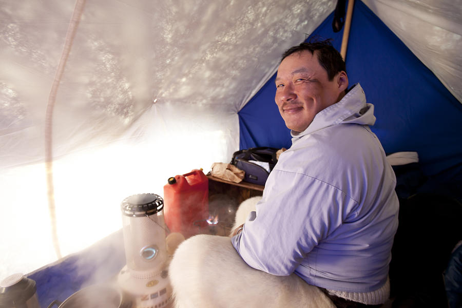 Inuit man smiles inside tent while camped on ice Photograph by Justin Lewis